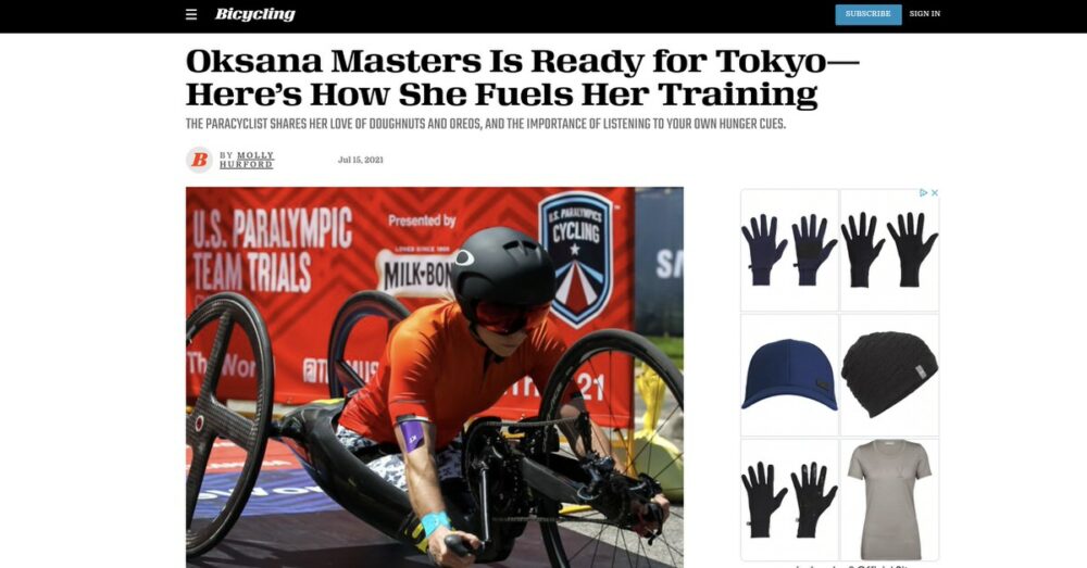 Headline reads, "Oksana Masters Is Ready for Tokyo—Here's How She Fuels Her Training." The photo includes a woman in an orange helmet and red shirt using a handcycle. Additional images feature gloves, a cap, and a t-shirt. 

Note: "Oksana Masters" is directly mentioned in the image, hence stated in the alt text.