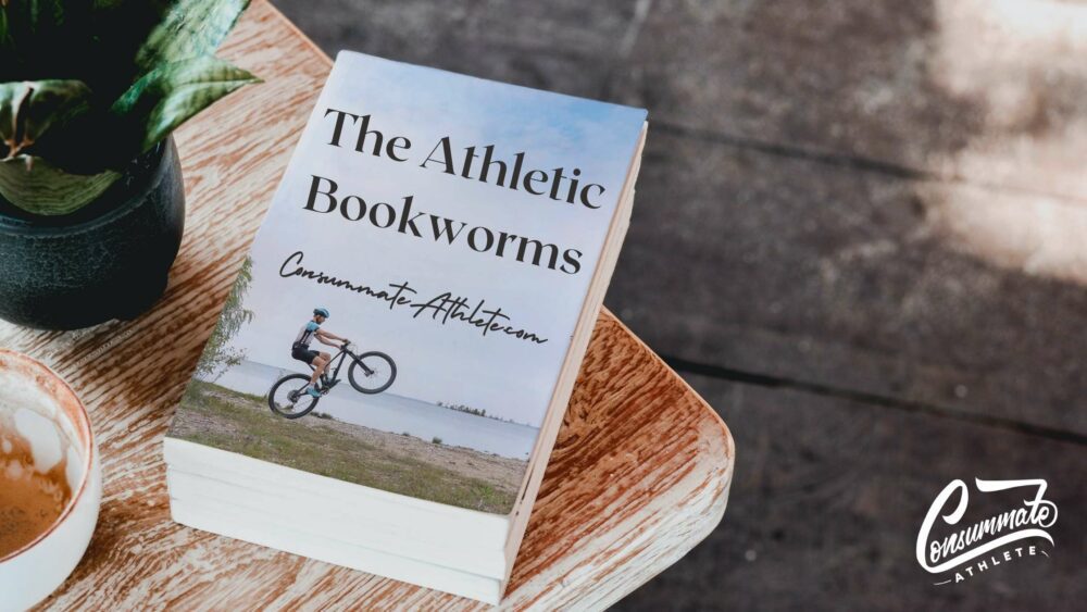 A book titled "The Athletic Bookworms" with an image of a person doing a wheelie on a bike is placed on a wooden table. A potted plant and a ceramic bowl with light-colored contents are also on the table. The logo "Consummate Athlete" is visible in the corner.