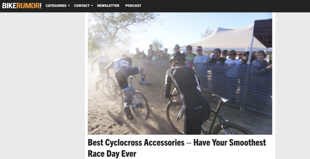 A cyclocross race is underway, with cyclists riding on a dirt path. Spectators stand behind a metal barrier on the right. The caption at the bottom reads, "Best Cyclocross Accessories — Have Your Smoothest Race Day Ever." The top header shows "BIKERUMOR!.