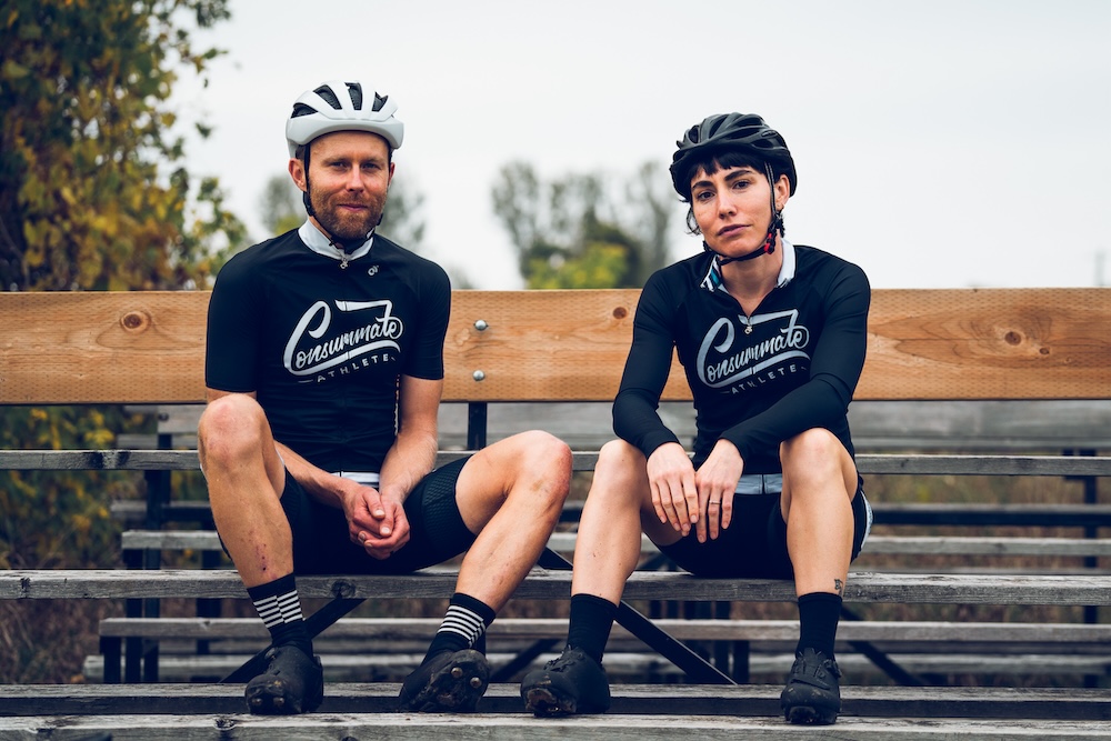 Two cyclists in matching athletic wear resting on wooden bleachers after a cycling training session.
