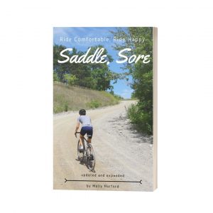 The image shows a book cover titled "saddle sore: ride comfortable, ride happy" by molly hurford. the cover features a cyclist riding on a rural road, with trees and a clear sky in the background.