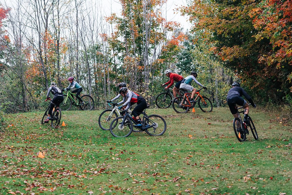 Group of mountain bikers preparing for bike coaching to navigate an obstacle course in a wooded area.