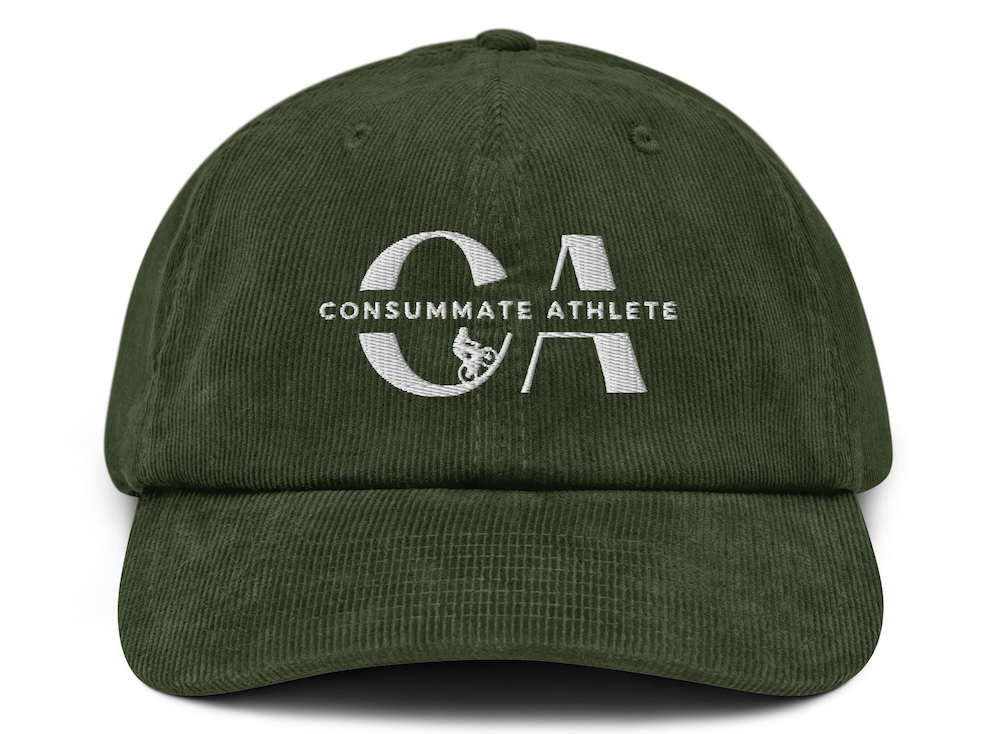 A green baseball cap with the words "consummate athlete" and a stylized letter 'a' embroidered in white on the front. the cap is viewed from the front on a white background.