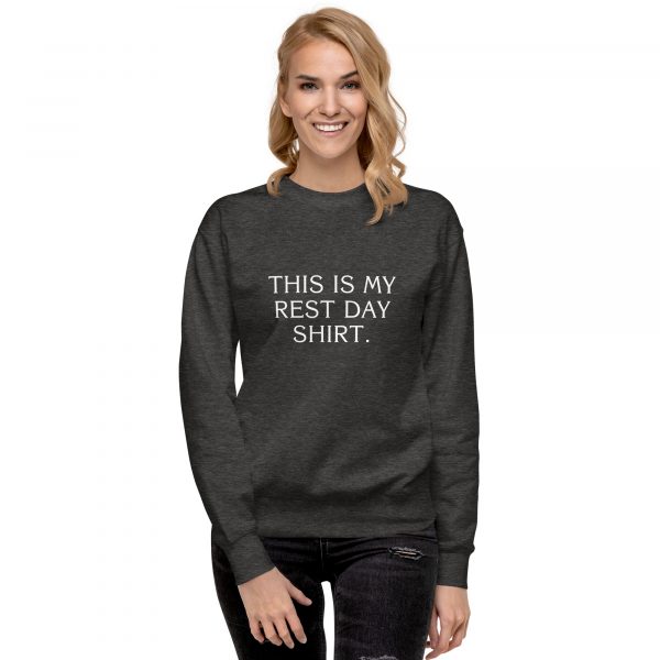 A person with long blonde hair smiles and wears a dark gray sweatshirt with the text "THIS IS MY REST DAY SHIRT" printed on it in white. The person is standing against a plain white background.